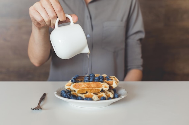 Cropped shot of woman pouring sweet syrup on tasty waffles