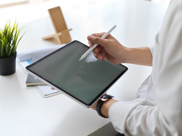 Cropped shot of young businessman writing on mock up tablet in modern office room