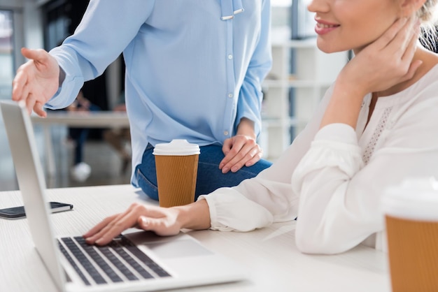 Cropped shot of young businesswomen working with laptop and talking in small business office