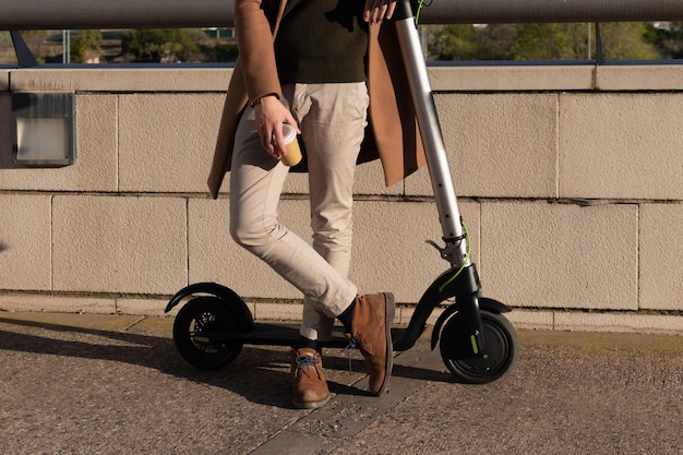 Cropped shot of young bussinesman resting on electric scooter from work with take away coffee cup on hand on spare time