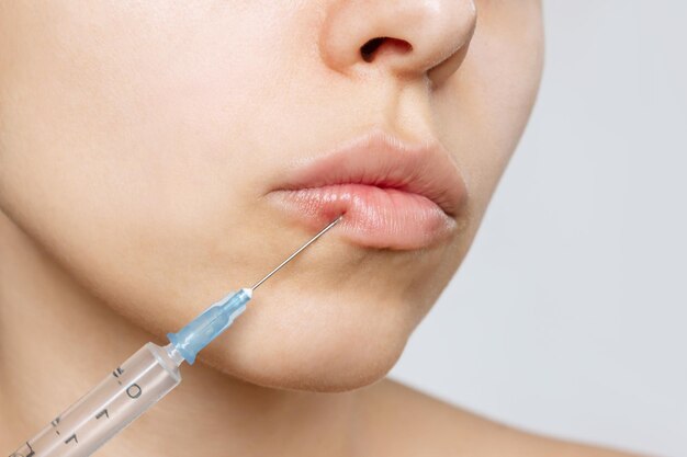 Cropped shot of young caucasian blonde woman's face with perfect lips with a syringe needle on lip