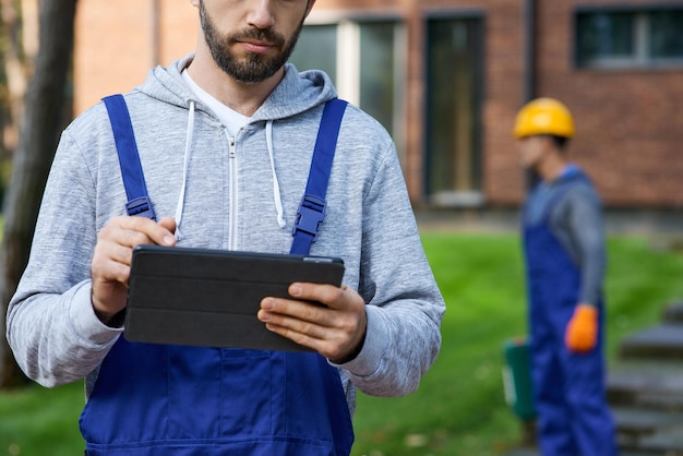 Cropped shot of young male builder holding digital tablet pc with coworker working in the