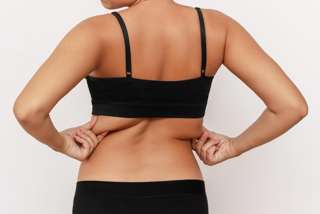 Cropped shot of a young tanned woman in black underwear holding fat folds on her back