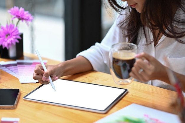 Cropped shot young woman holding coffee cup and working with digital tablet in creative office