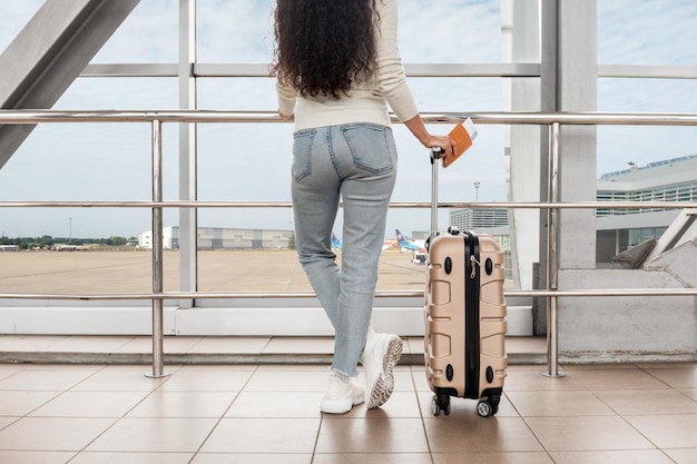 Cropped shot of young woman standing with suitcase near airport window