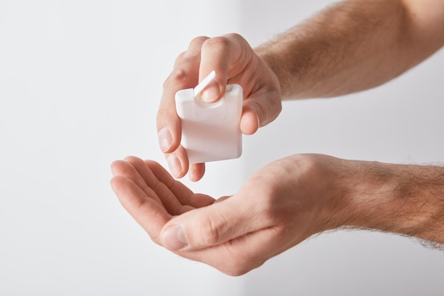 Cropped view of adult man using hand sanitizer on white background