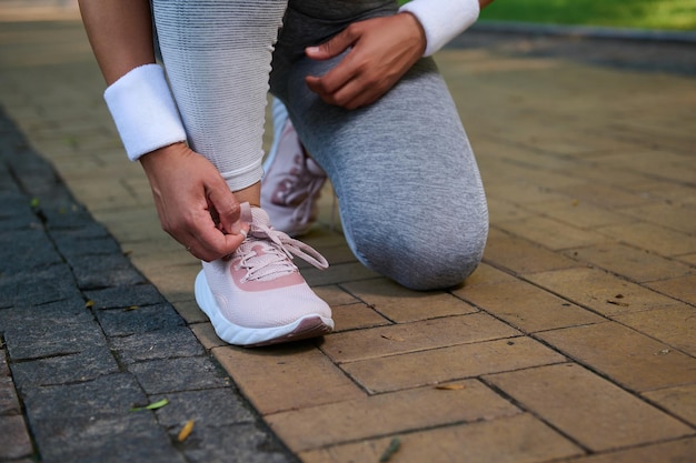 Cropped view of a female athlete runner tying shoelaces on her sneakers getting ready for jog along the treadmill of a city park