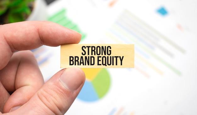 Cropped view of hands holding wooden cube with STRONG BRAND EQUITY lettering on work table. Top view