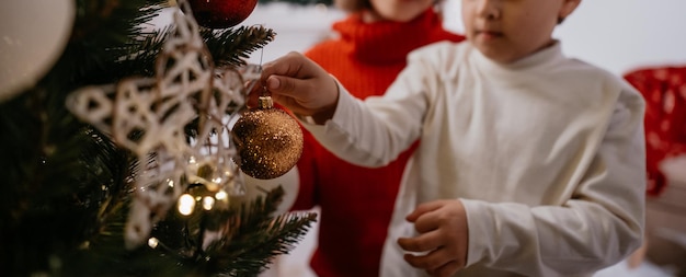 Cropped view of happy boy decorating Christmas tree with his mother during cozy home evening