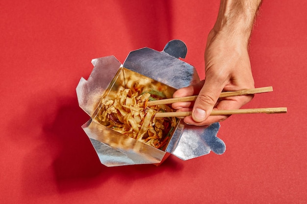 Cropped view of man holding chopsticks near spicy noodles on red