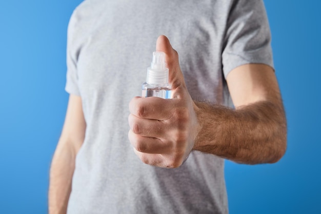 Cropped view of man holding gel hand sanitizer in bottle isolated on blue