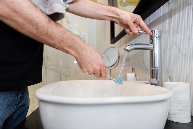 Cropped view of man holding toothbrush under water in bathroom