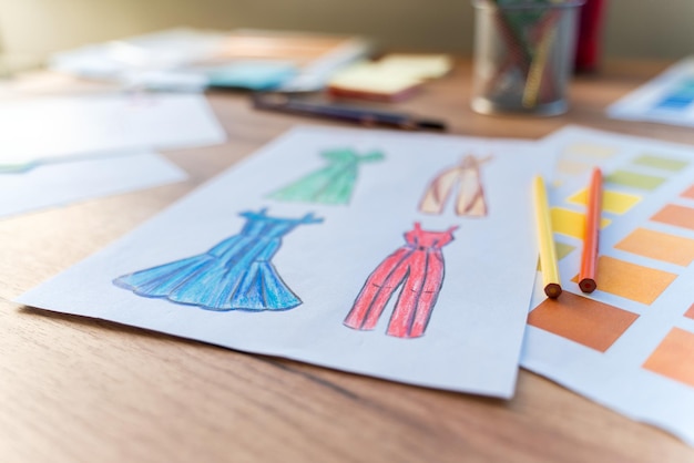 Cropped view of the sketches of clothes and color samples laying on the wooden table. Creative atmosphere concept