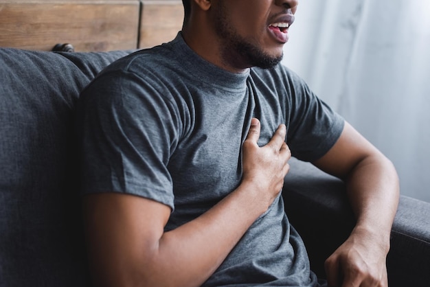 Cropped view of stressed african american man having heart attack at home