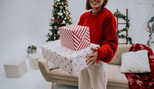 Cropped view of unrecognizable woman carrying Christmas presents near fir tree at the cozy apartment