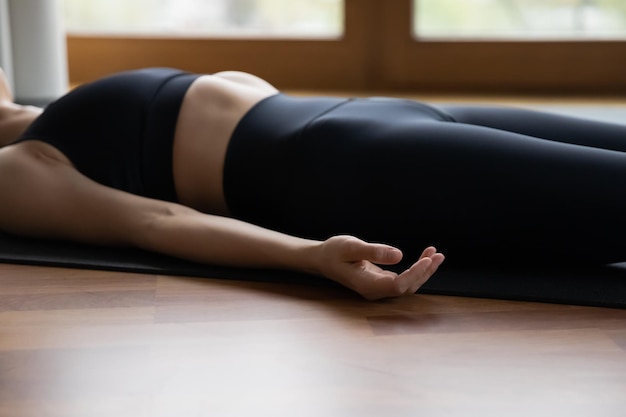 Photo cropped view woman in black sportswear lying on mat in savasana corpse pose asana in hatha yoga for relaxation at end of session exercise calms mind reduces stress fatigue after practice concept