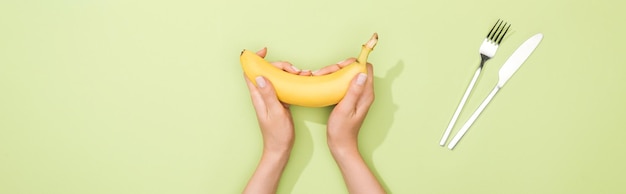 Cropped view of woman holding banana in hands near fork and knife