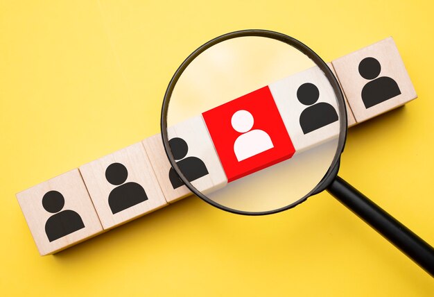 Cropped view of woman holding magnifying glass under wooden cubes with logo on yellow background