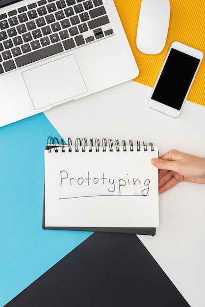 Photo cropped view of woman holding notebook with prototyping lettering near laptop smartphone computer