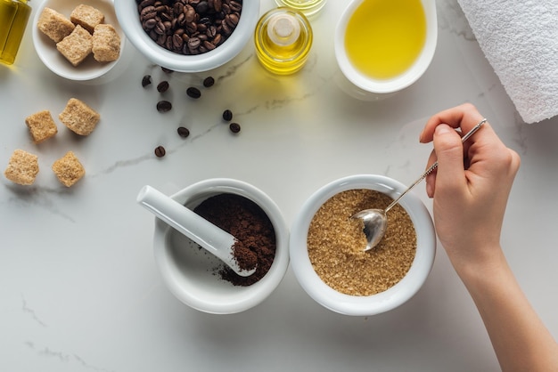 Cropped view of woman holding spoon with brown sugar pounder with ground coffee and various