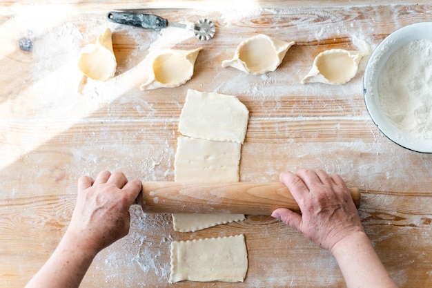 Cropped view of the woman using roller pin while making bakery from dough at the wooden table with flour Bakery concept