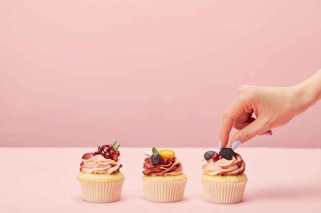 Photo cropped view of woman with sweet cupcakes with fruits and berries isolated on pink