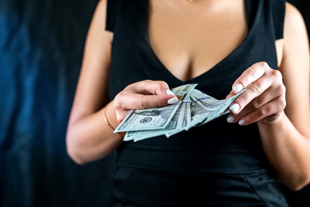 Cropped view of young sexy woman in black dress counting US dollar money in hands dollars in the hands of a woman a selfsufficient woman with money