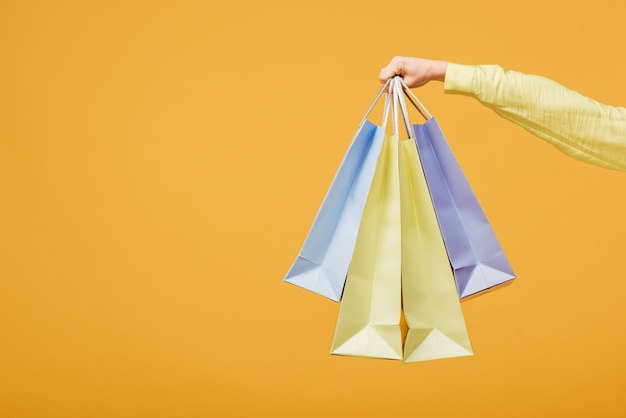 Cropped view of young woman holding shopping bags isolated on yellow