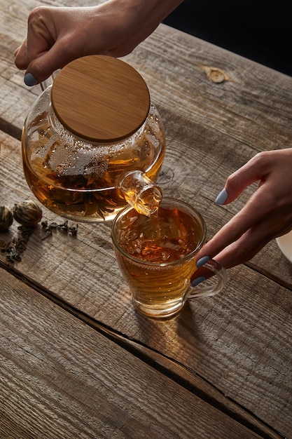 Cropped view of young woman pouring chinese blooming tea in cup on wooden table