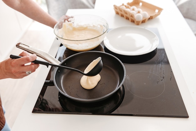 Cropped woman cooking in kitchen at home, and frying pancakes on modern stove