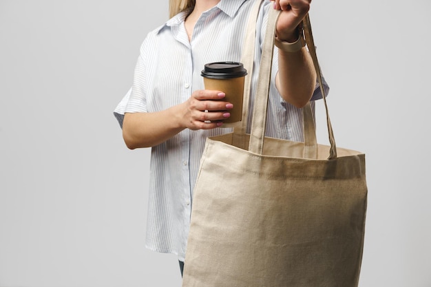 Cropped woman with cotton bag and paper coffee cup studio shot