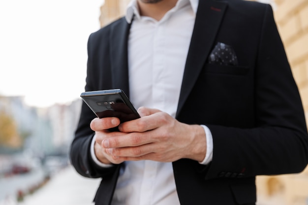 Cropped a young businessman wearing suit standing at the city, using mobile phone