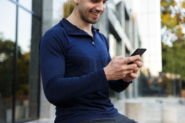 Croppped image of a sportsman using mobile phone while sitting outdoors