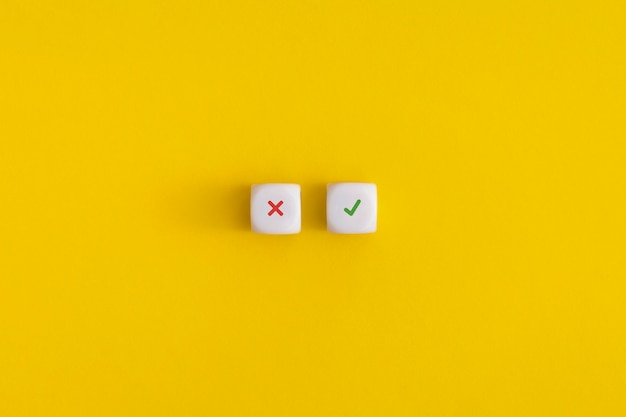 Cross and check mark on a white cubes on yellow background. Approving, voting or right decision concept.