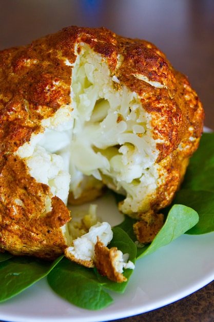 Cross section of a seasoned and cooked head of cauliflower on a bed of greens