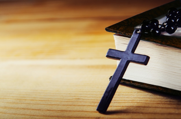 Cross on a thread with black beads with a bible on a wooden table.