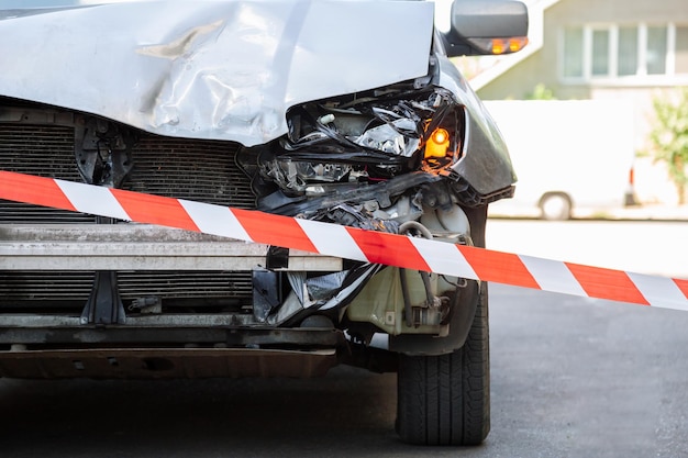 Crossed red white warning tape in front of destroed car accident broken hood of car on road fenced