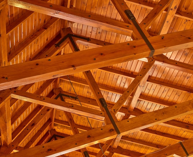 Crossed wood support trestles with their angle supporters on a ceiling Closeup of roof rafters and cross beams of a shelter Crossed thick beige crossbeams boards for building and construction