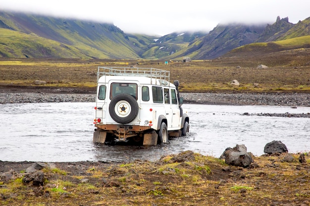 Crossing a tourist jeep car across a mountain river on the road Stormy mountain river flows from glaciers in Iceland