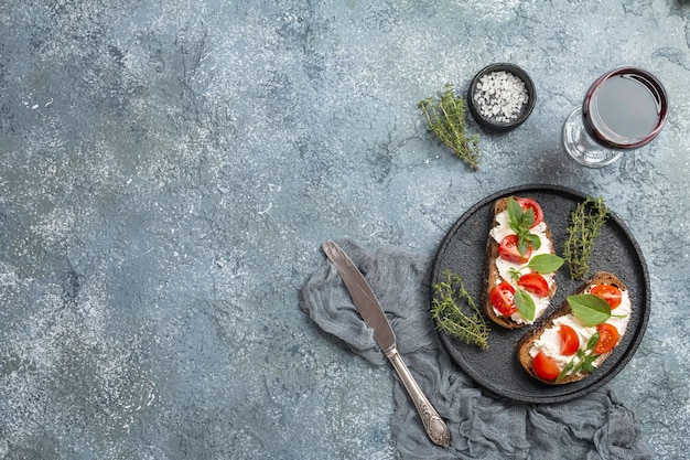 Crostini appetizers with cherry tomatoes basil and cheese on gray