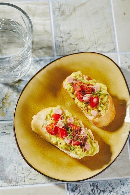 Crostini or bruschetta with softened avocado ham and tomatoes toast with mashed avocado