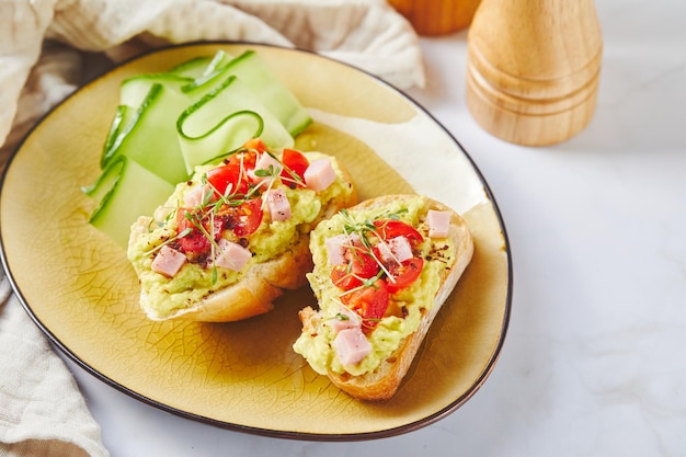 Crostini or bruschetta with softened avocado ham and tomatoes toast with mashed avocado