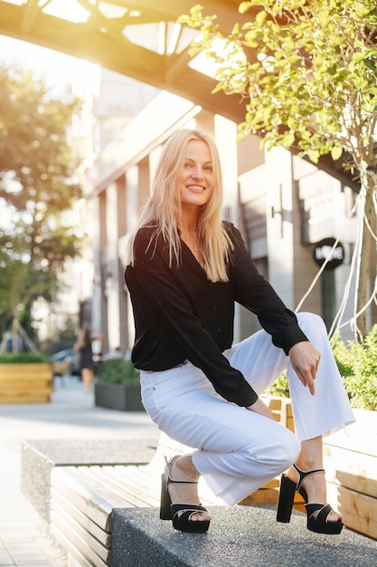 Crouching attractive young blond woman in white pants posing for a photo