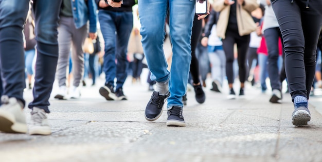 A crowd of people walking on the sidewalk some holding phones and looking at their screens