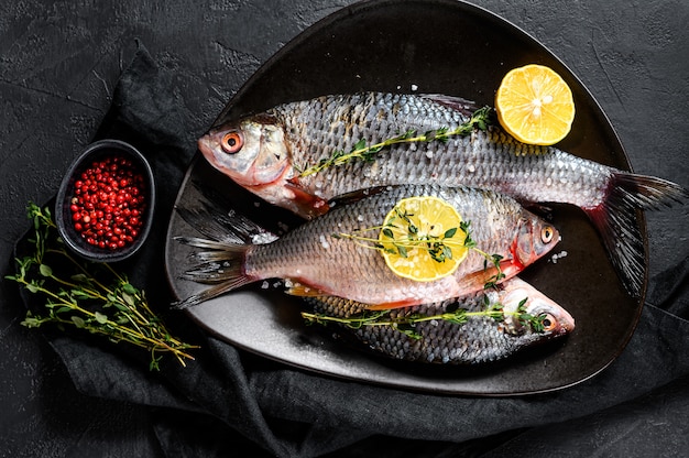 Crucian carp with lemon and thyme on a black plate. River organic fish. Top view