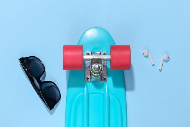 Cruiser board and wireless headphones, sunglasses on a bright blue background. 