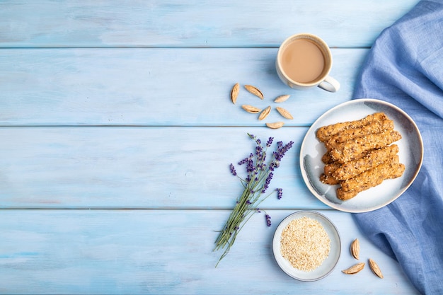 Crumble cookies with seasme and almonds on ceramic plate with cup of coffee on blue wooden background top view copy space