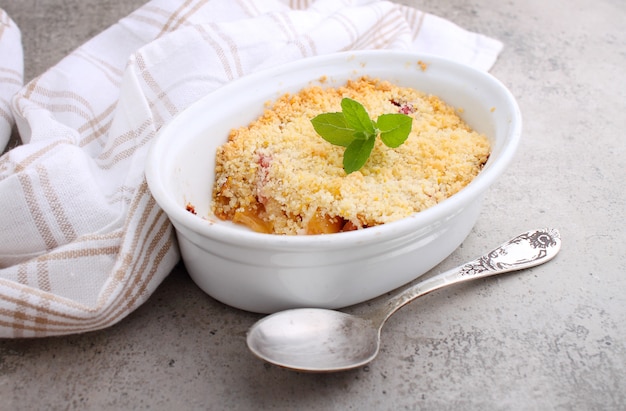 Crumble with strawberries and apples on a white plate and concrete table.