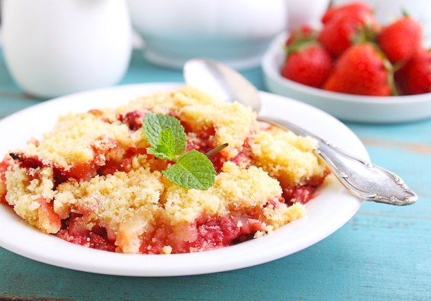 Crumble with strawberries in white plate on a blue background