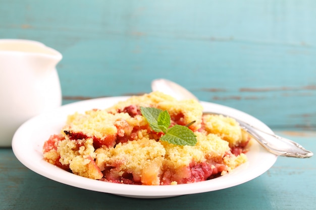 Crumble with strawberries in white plate on a blue background